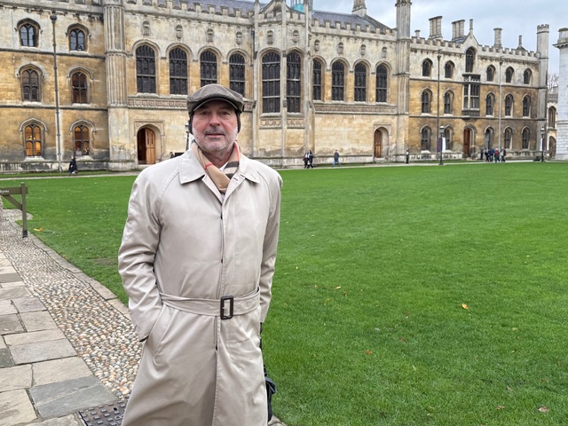 Mauricio at Cambridge, trench coat and cap, collegiate setting