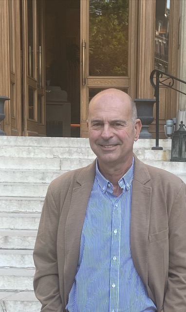 Mauricio in blue striped shirt and tan jacket, seated on stone steps