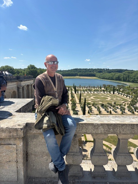 Mauricio seated on a balustrade at Versailles, the gardens behind